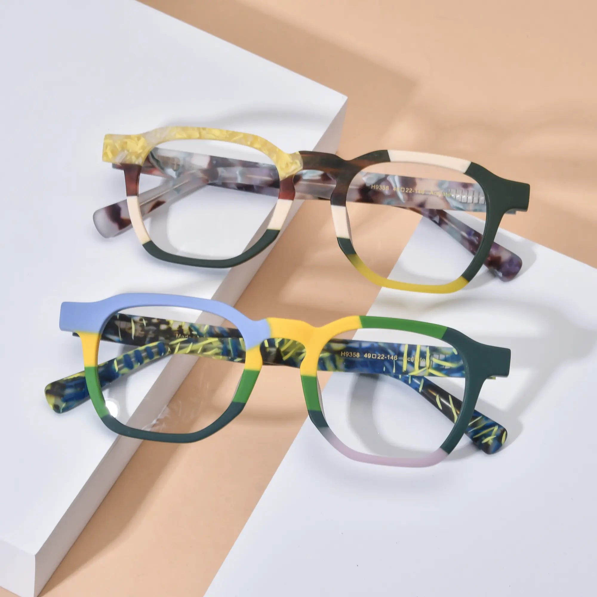 Lifestyle flatlay image showcasing VoyueLens™ VL19358 colorblock square glasses in both Citrus Fade and Ocean Tortoiseshell variants, styled on a soft neutral background to highlight vibrant frame contrasts and artistic acetate detailing.